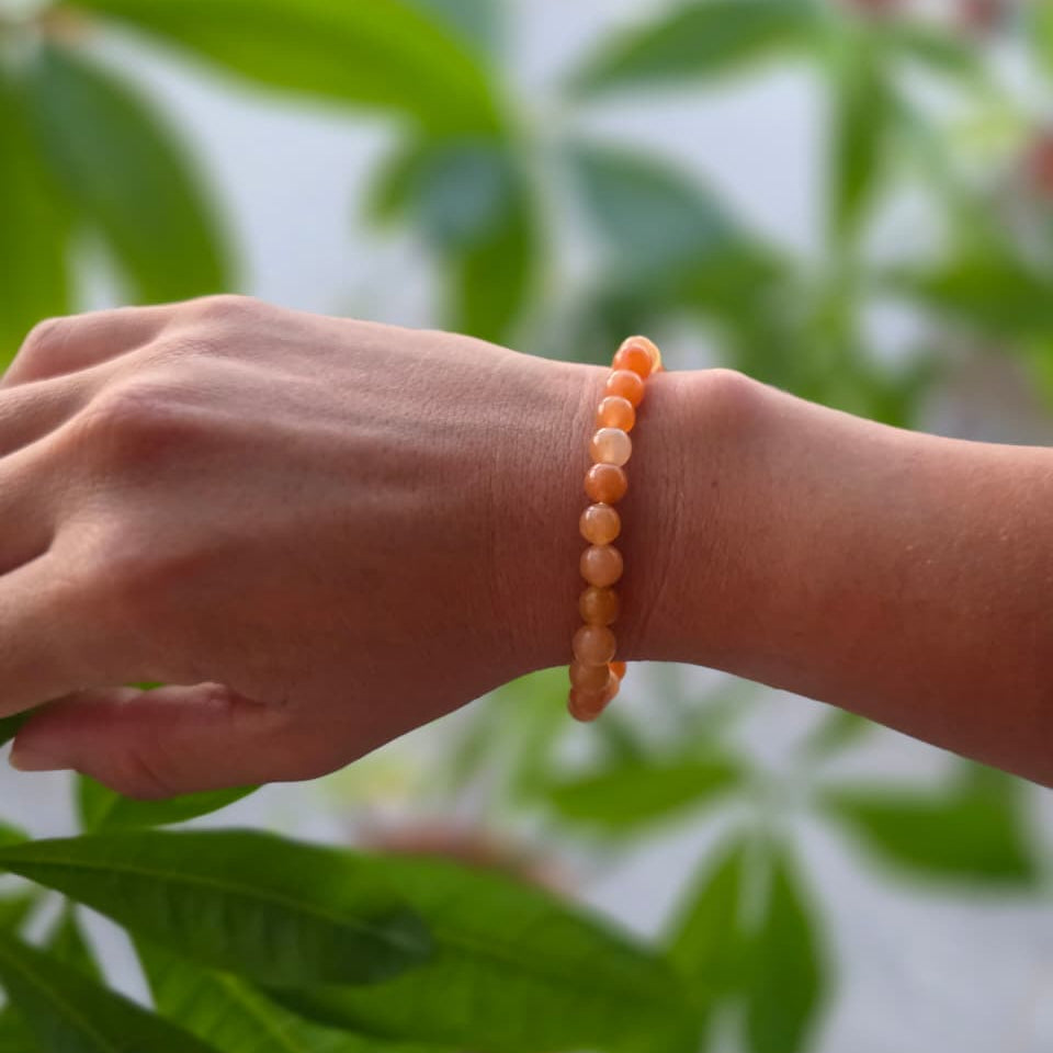 Pulsera de aventurina naranja natural de 6 mm llevada en la muñeca, con piedras en tonos naranjas y cálidos, diseño elegante y natural