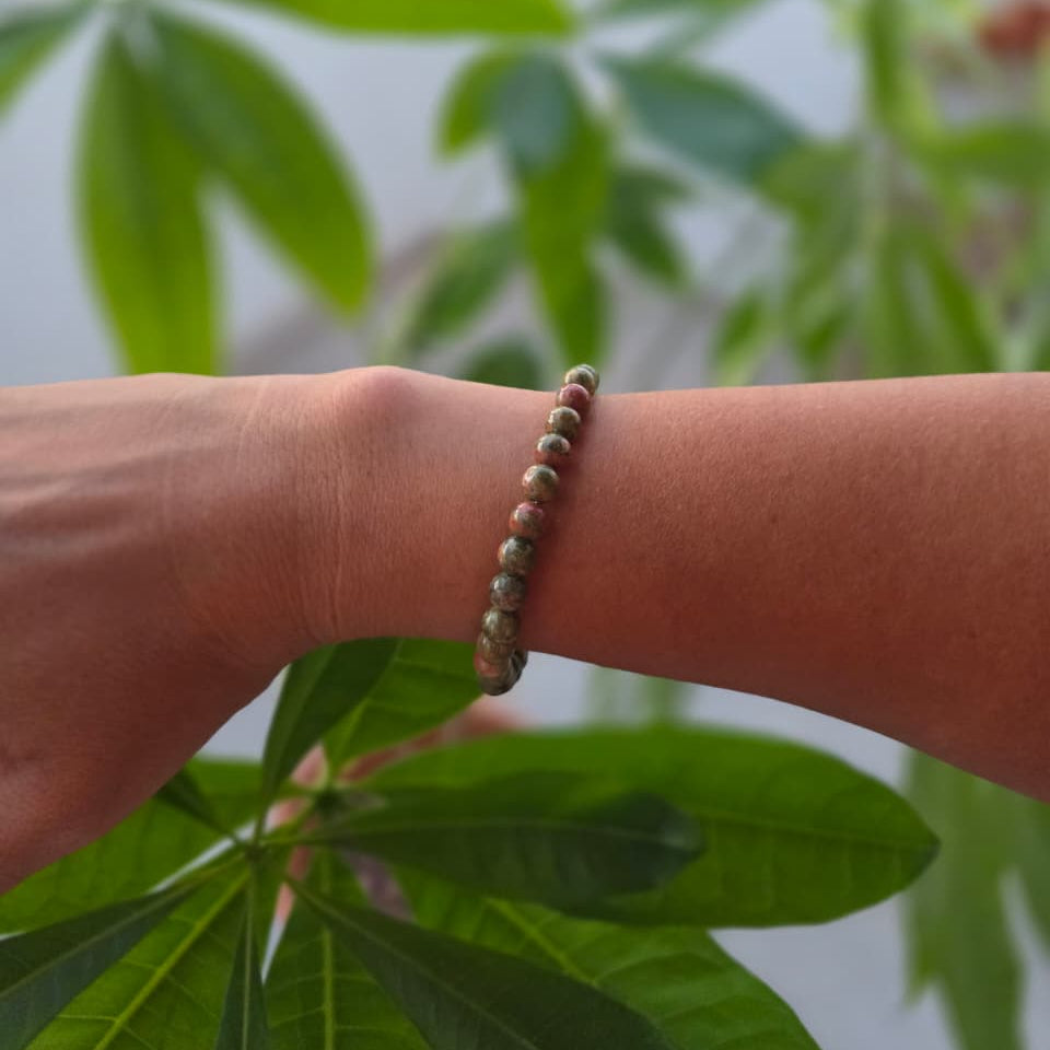 Pulsera de unakita natural de 6 mm llevada en la muñeca, con piedras en tonos verdes y rosados, patrones naturales y diseño elegante