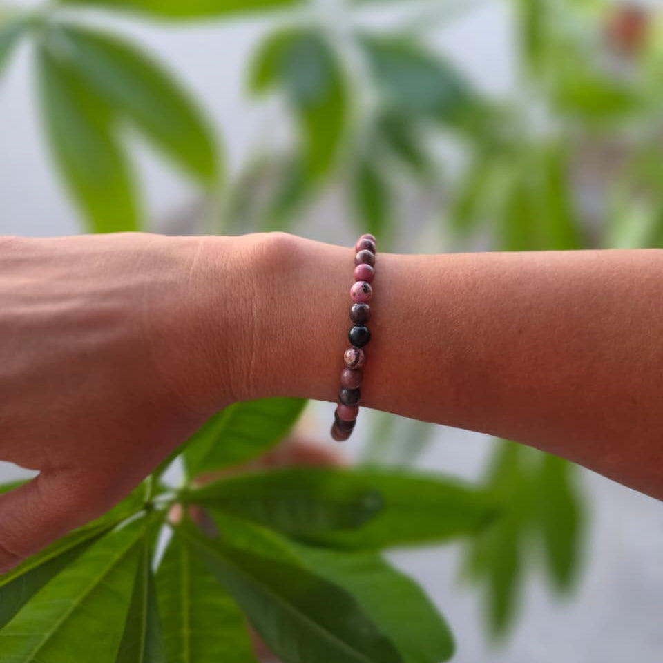 Pulsera Black Line de rodonita natural de 6 mm llevada en la muñeca, con piedras rosadas y vetas negras, diseño elegante y distintivo