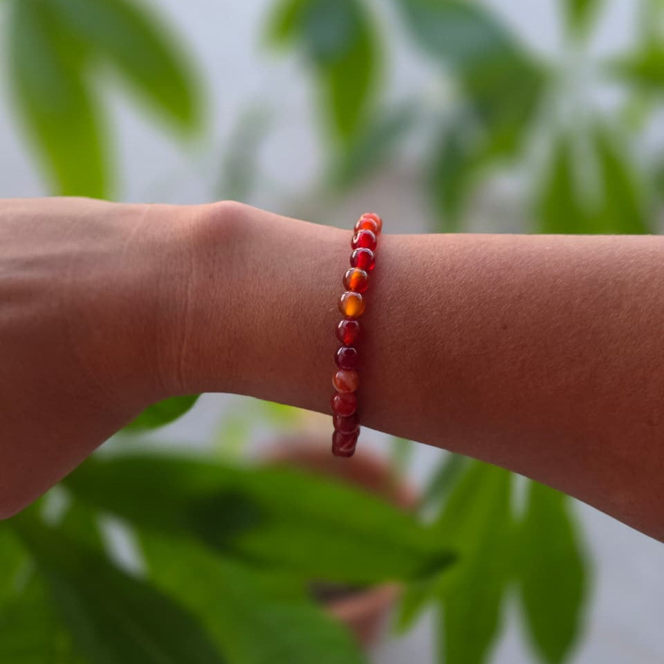Pulsera de cornalina natural de 6 mm llevada en la muñeca, con piedras en tonos naranjas y rojizos, diseño elegante y natural