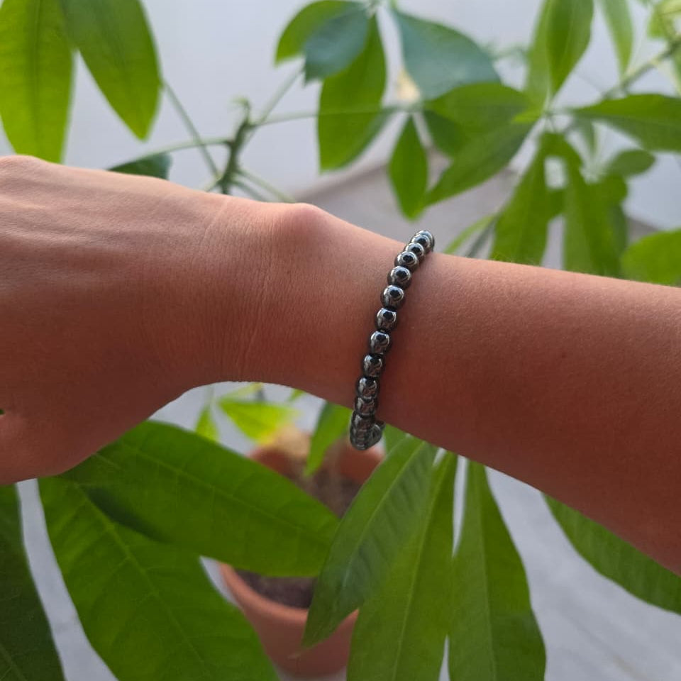 Pulsera de hematita natural de 6 mm llevada en la muñeca, con piedras en tonos gris metálico y negro, diseño elegante y minimalista