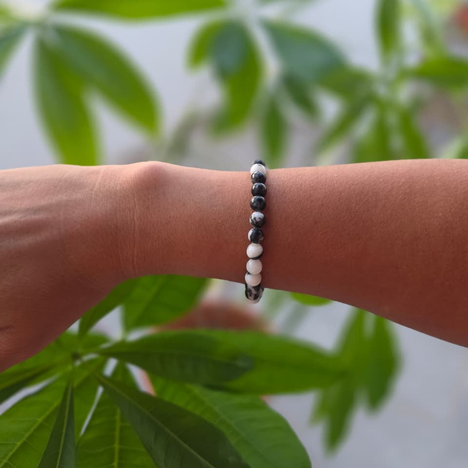 Pulsera de jaspe cebra natural de 6 mm llevada en la muñeca, con piedras en tonos blancos, grises y negros, diseño único y elegante