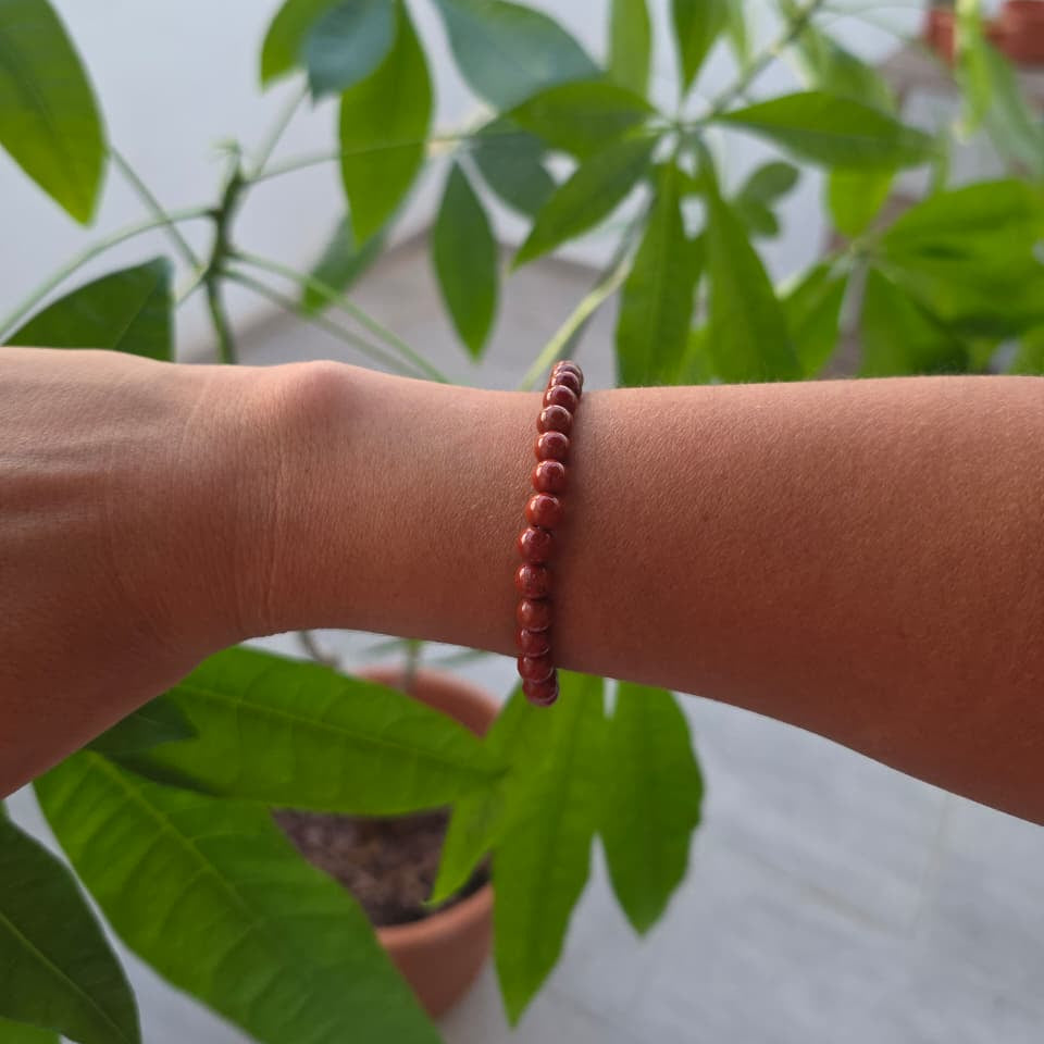 Pulsera de jaspe rojo natural de 6 mm llevada en la muñeca, con piedras en tonos rojos y tierra, diseño elegante y natural