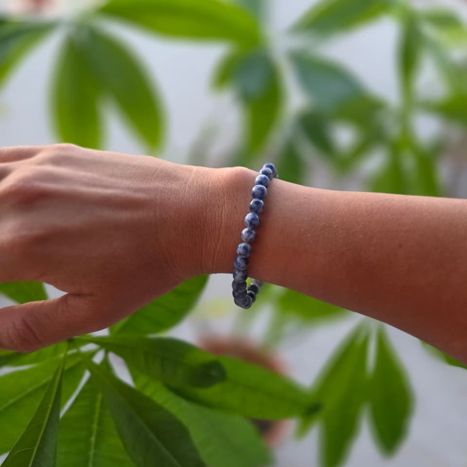 Pulsera de sodalita natural de 6 mm llevada en la muñeca, con piedras en tonos azules y blancos, vetas naturales y diseño elegante